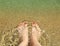 Woman`s feet on the sand beach with crystal transparent waves. Sy