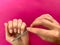 Woman`s girl`s hand filing nails with metal nail file on a pink background. Self manicure