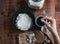 A woman`s hand adding yeast to water for making sourdough. Bowl with flour and yeast on paper Bakery concept. Top view