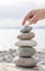 Woman& x27;s hand balancing a stack of stones on a driftwood beach log.