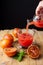 Woman`s hand with bottle, serving blood orange juice in a glass cup on rustic table with oranges and mint, vertical black backgro