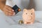 a woman\\\'s hand with a credit card and a piggy bank, next to a calculator on the table. crisis and inflation. Cost