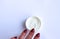 A woman`s hand with a crimson manicure and a white jar with a greasy cosmetic cream on a white background.