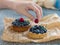 A woman`s hand decorates tartalets lying on mint paper with fresh raspberry berries.