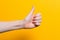 A woman`s hand gives a thumbs up. Close up. Yellow background. Copy space