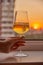 A woman& x27;s hand with a glass of wine on the background of a bright sunset.