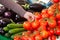 A woman\'s hand grabs a bunch of tomatoes from a market stall