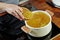 Woman`s hand hold a wood bowl with raw noodles to put it into the boiling bouillon. Opened white saucepan on the black stove.