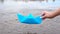 Woman`s hand holding blue paper boat over the river