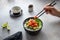 Woman`s hand holding chopsticks with a slice of salmon and eating a hawaiian poke bowl.