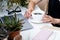 Woman`s hand holding cup of coffee in cozy summer office with laptop and green plants