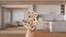 Woman\'s hand holding daisies, spring and flowers idea, over japandi wooden kitchen and living room, white interior design
