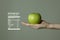 Woman`s hand holding green apple, nutrition facts on grey background.