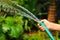 A woman`s hand holding green water hose watering the plants and flowers at the garden - botanical, ecological and environmental co