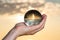 Woman`s hand holding high grade Clear Quartz Sphere at the sunrise in front of the lake