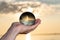 Woman`s hand holding high grade Clear Quartz Sphere at the sunrise in front of the lake