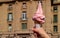 Woman`s Hand Holding Pink Soft Serve Ice Cream Cone against Vintage Buildings