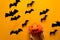 Woman`s hand holding pumpkin with scary smile and black paper bats flying on yellow background