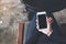 A woman`s hand holding white mobile phone with blank desktop screen on thigh in cafe