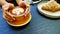 Woman`s hand holding yellow cup of art latte coffee with almond cream croissant, knife, fork and black phone for background