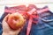 A woman`s hand holds an Apple against the top of a pair of denim trousers on a wooden background. Blue jeans with a measuring tap