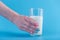 A woman\'s hand holds a glass of fresh milk against a blue background. Concept of healthy dairy products with calcium