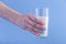 A woman\'s hand holds a glass of fresh milk against a blue background. Concept of healthy dairy products with calcium