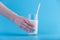 Woman\'s hand holds glass of fresh milk with a straw on a blue background. Concept of healthy dairy products with calcium