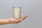 A woman`s hand holds in the open palm a glass of fresh milk against a white background. minimalism. The concept of healthy dairy