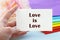 A woman`s hand holds a piece of paper with the inscription Love is love, against the background of a stack of cloth folded in the