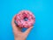 A woman`s hand holds a pink donut on a blue background. Confectionery products. Harmful fast food