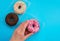 A woman`s hand holds a pink donut on a blue background. Confectionery products. Harmful fast food