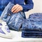 A woman`s hand holds a stack of clean folded ironed things made of blue cotton denim on the Ironing Board and an iron