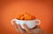 A woman`s hand holds a white bowl full of round sliced carrots. Orange background