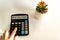 A woman`s hand lies on a calculator with text of New Solutions on the display and on a white background next to the catus flower.