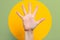 A woman`s hand with outstretched fingers. Green background with a yellow circle. Close up. The concept of hypnosis, influence, an