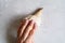 A woman`s hand with pale pink painted nails holds a seashell on a gray concrete background