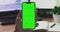 A woman\'s hand phone with green mock-up screen chroma key holds a smartphone of the workspace background. Stock