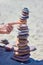 A woman's hand points or pushes a tall cairn on a sandy beach