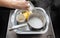 A woman& x27;s hand pours hot water into a basin with dirty dishes and environmentally friendly oxygen bleach. Washing