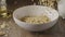 Woman\'s hand pours natural granola into ceramic bowl against dar