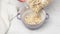 A woman`s hand pours oatmeal from a transparent plastic bag into a round ceramic plate