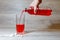 A woman\'s hand pours a red sports drink or lemonade into a glass Cup from a plastic bottle. Energy drink in glass and plastic bot