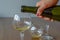 Woman`s hand pours white wine into a glass against blurred broke