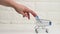 A woman`s hand pushes an empty miniature metal shopping cart on a white table. Online shopping concept