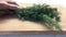 Woman\'s hand puts a bunch of dill on a wooden board