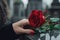 Woman\\\'s hand puts a red rose on a black granite tombstone outdoors. Funeral ceremony