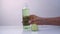 A woman's hand puts, takes on a white table a transparent bottle with a refreshing face tonic from a cucumber, in the