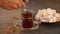 Woman`s hand puts turkish tea in traditional glass cup on the wooden table. Oriental.