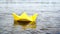 Woman`s hand putting yellow paper boat on the water and pushing it away